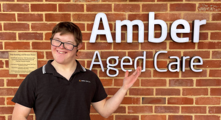 Joseph Brady smiling beside a sign that says 'Amber Aged Care'.
