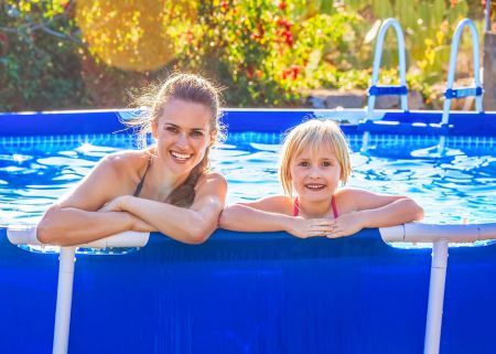 A mother and daughter hanging over the edge of a temporary above ground pool and smiling.