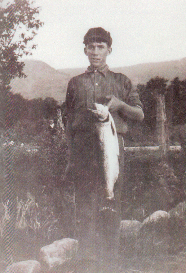 A boy holding a large fish he has caught in the river.