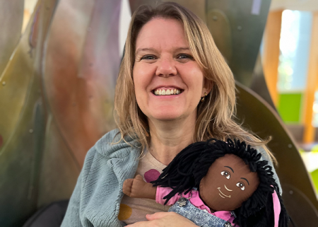 A library staff member smiling and holding a doll.