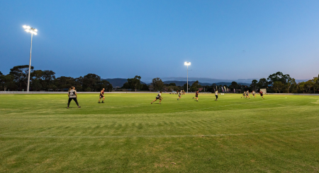 Football players playing on an oval at dusk.