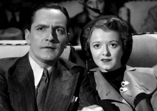 A black and white photo of a man and a woman watching a movie.