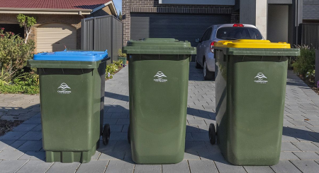 Three wheelie bins sitting on the kerb out the front of a house ready for collection.