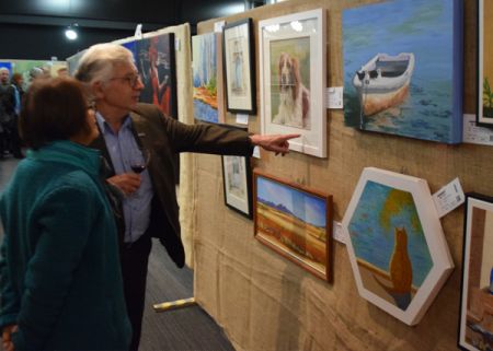 A man and woman looking at paintings at the Campbelltown Art Show.