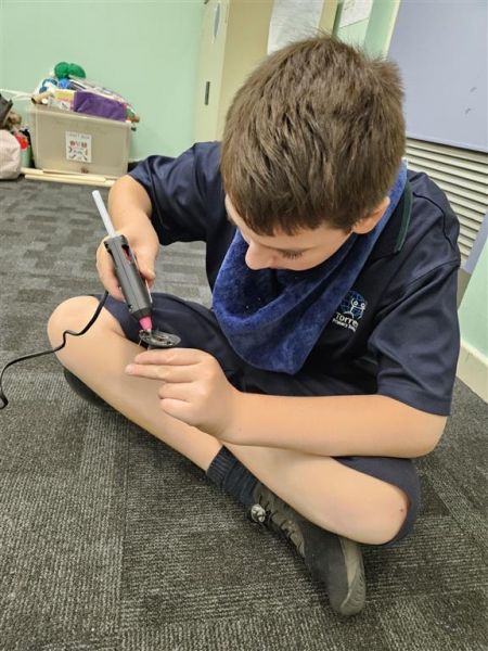 Jayden creating works of art using a glue gun and collected plastic, metal and rubber.